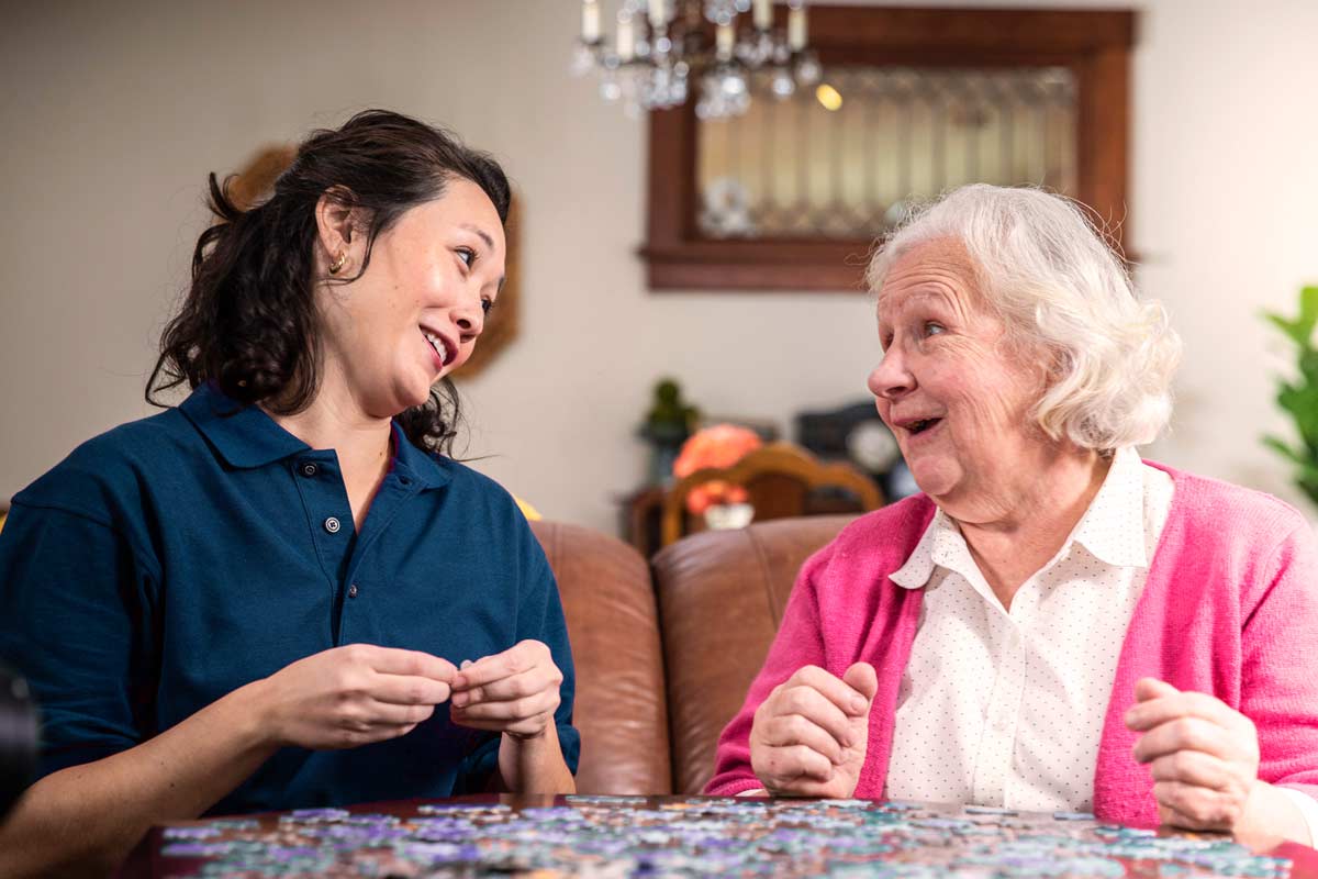 Aging woman and Care Professional work on puzzle together at home