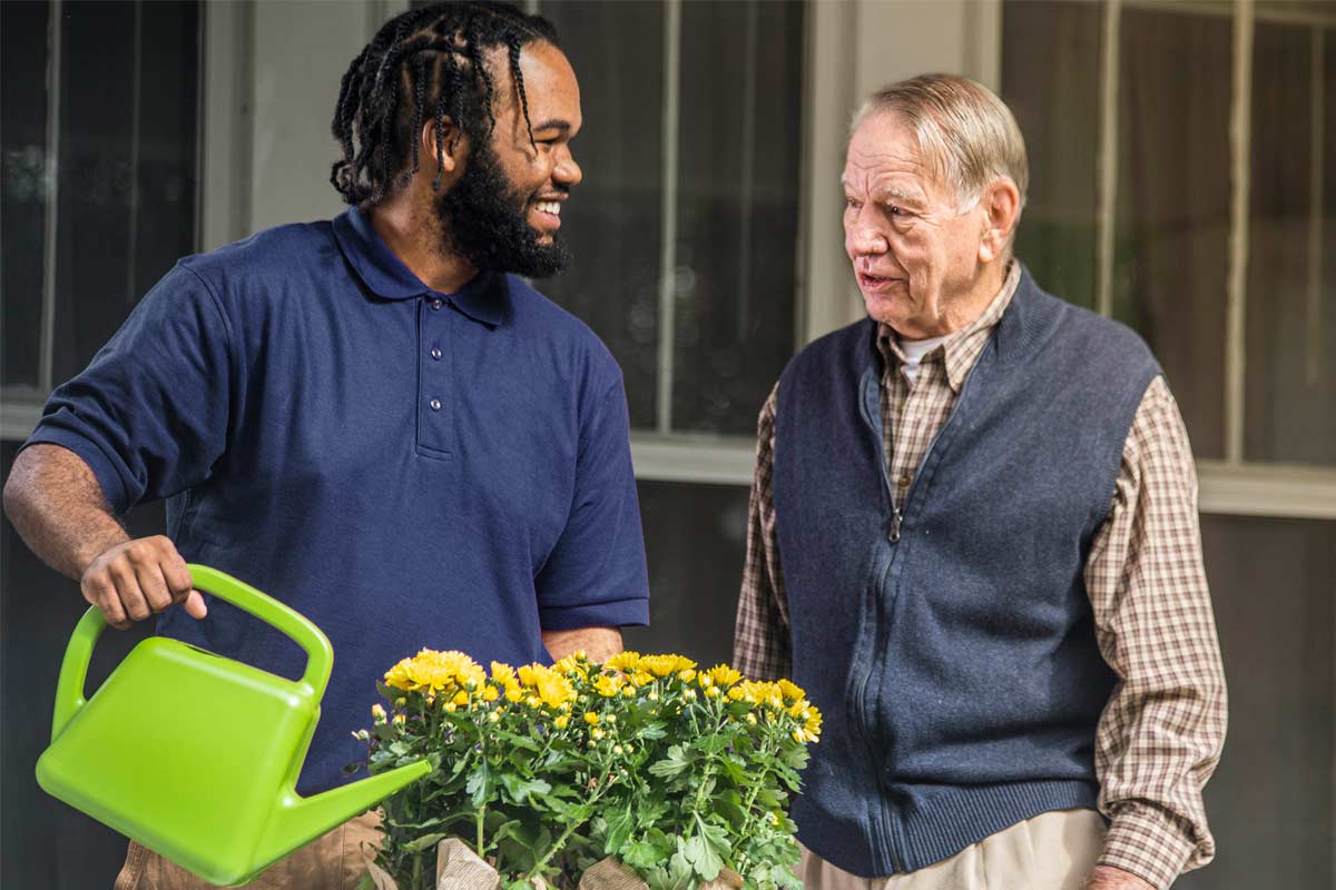 Care Professional and aging man water flowers outside