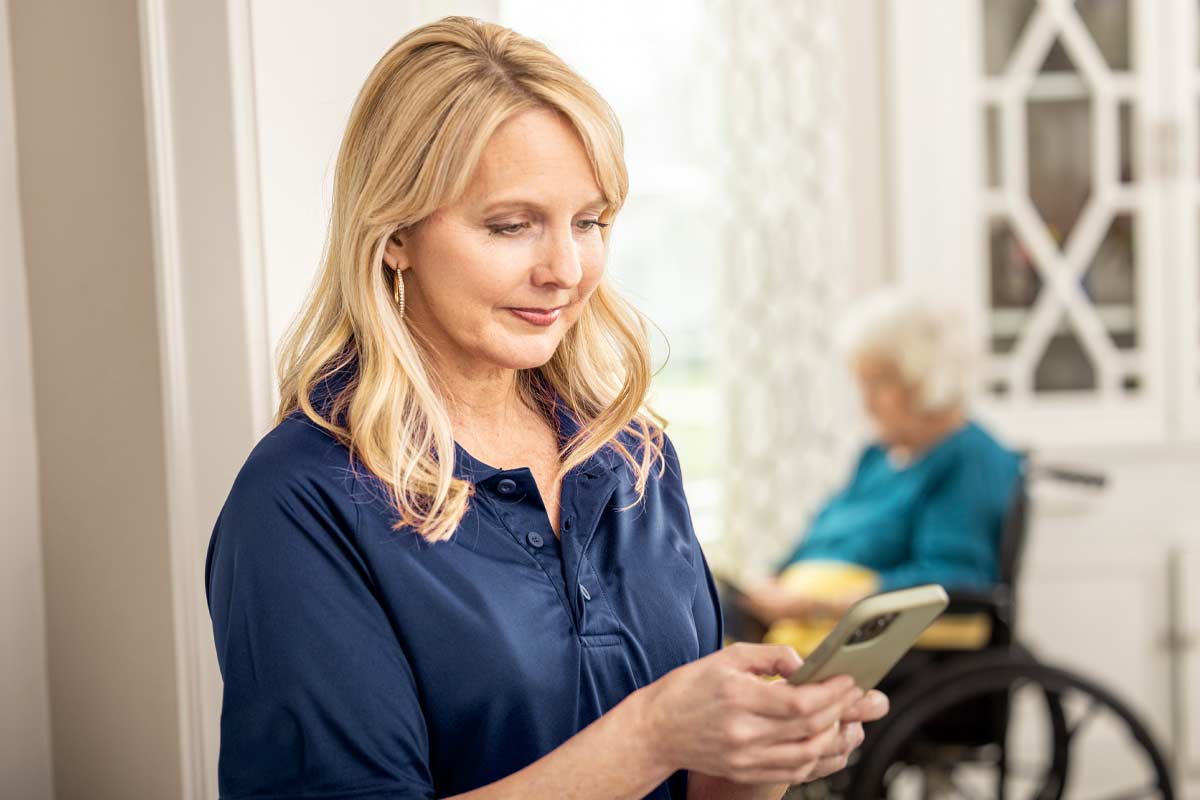 Care Professional reviews mobile app with senior woman sitting in background