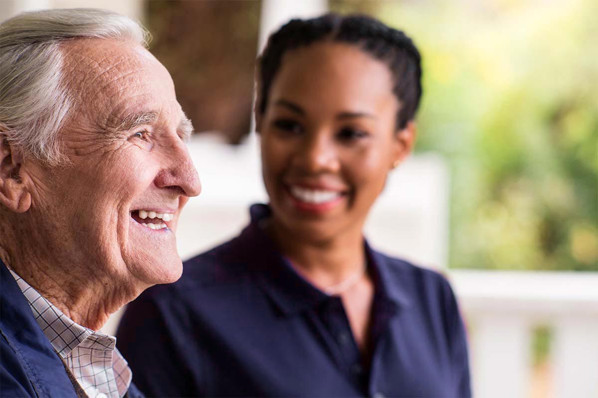 Senior man laughs with Care Professional in background